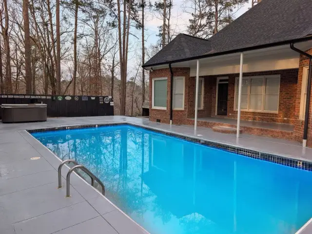 Light coated pool surround behind a brick home
